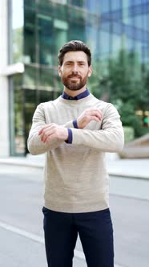 Vertical video. Portrait of confident businessman smiling with arms crossed stands outside on city