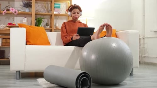 Woman Relaxing on Sofa with Tablet and Exercise Ball