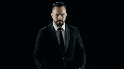 Man in Suit Performing Card Trick on Black Backdrop