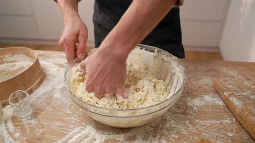 Person Kneading Dough in Bowl on Wooden Table
