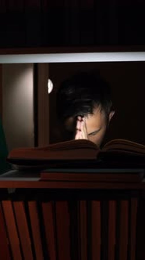 Vertical Video Student Praying with Open Book on Bookshelf at Night