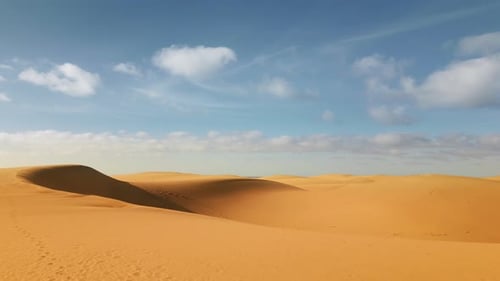 Gliding above vast golden sand dunes in the desert. The sweeping dunes contrast against a blue sky d