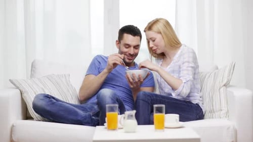 Young Couple Share Cereal on White Couch