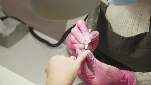 Up View of Nail Technician in Pink Gloves Using Black Electric File on Client Nail