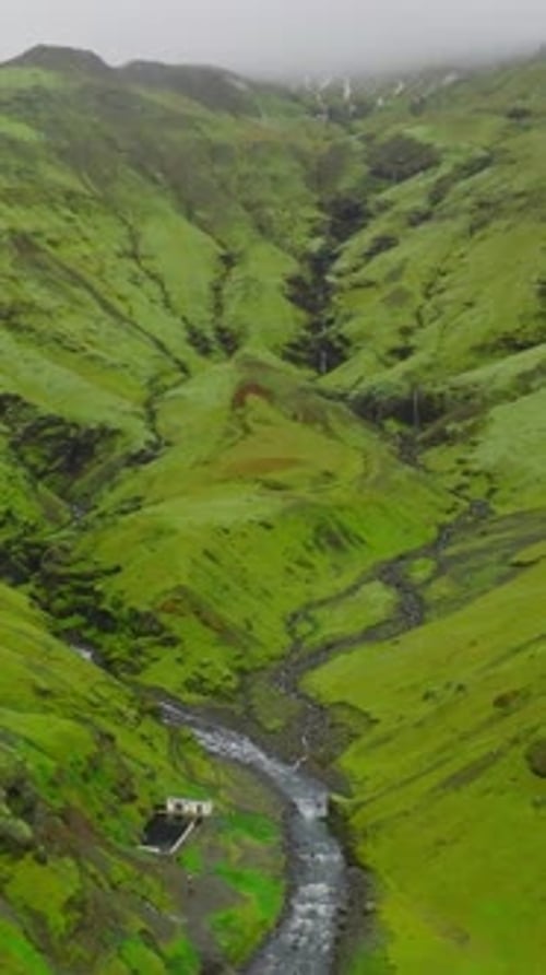 vue Vidéo verticale d'une rivière dans les montagnes avec des nuages au sommet avec les bains chauds de Seljavallalaug