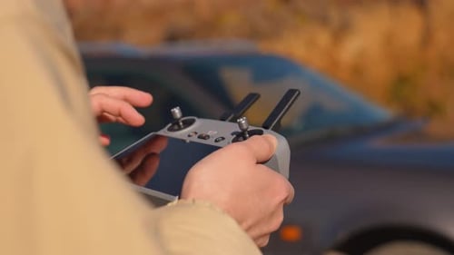 drone pilot with remote control in hands, controls quadcopter in field outdoors.