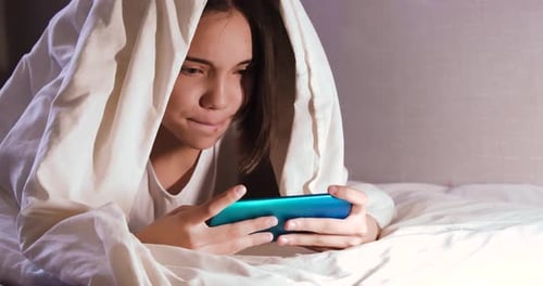Teen girl smiling using smartphone in bed