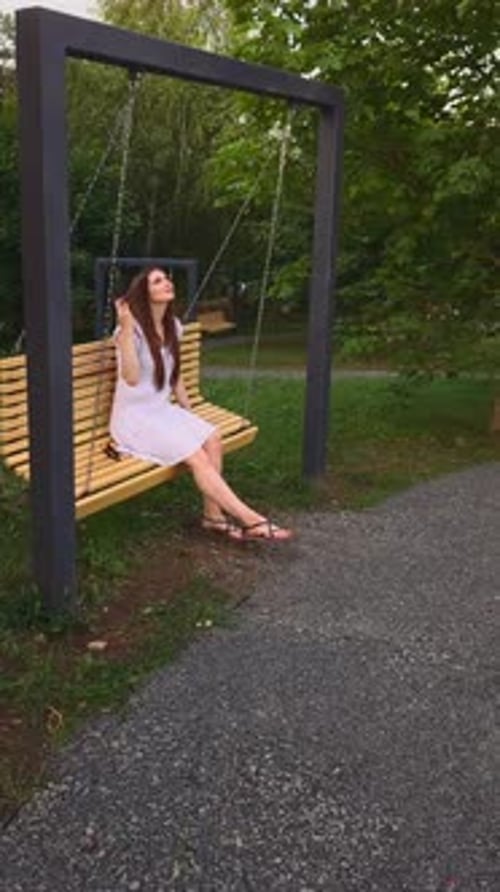 Young Woman Carelessly Swinging On Swing In City Park