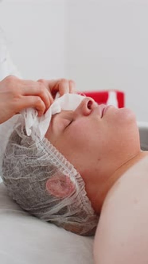 Cosmetologist Doctor Wipes Woman Face and Neck Cleaning Procedure with Cotton Pads in Beauty Clinic