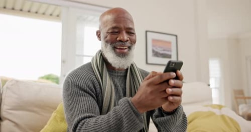 Senior Man Smiles While Using Smartphone at Home