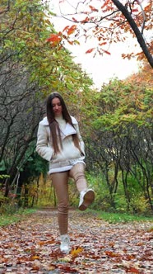 Attractive young woman walking down the park. Pretty lady walking by in autumn street.