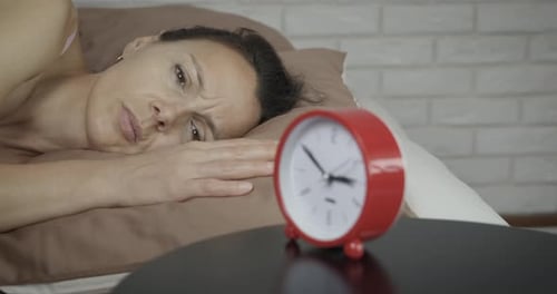 Woman Lying in Bed Next to Red Alarm Clock