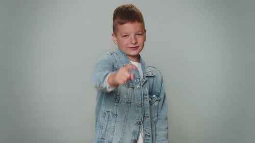 Kleiner Junge zeigt in die Kamera und schaut mit verspieltem, glücklichem Gesichtsausdruck, der eine Wahl trifft Hey du