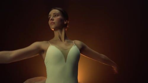 Elegant ballerina dances in dramatic lighting studio setting