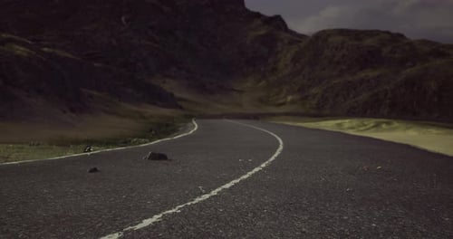 Curving Road Through Mountainous Landscape Under Cloudy Sky at Dusk