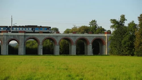 Slow motion railway viaduct with a passing passenger train crossing the bridge.