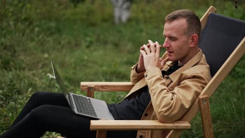 Man Works on Laptop in Chair Outdoors