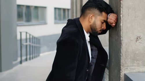 Man Stands Outdoors, Leans Head on Pillar