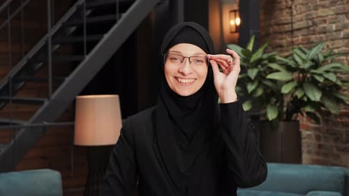 Lächelnde arabisch-muslimische Frau im schwarzen traditionellen Hijab blickt direkt in die Kamera