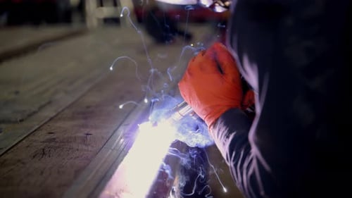 Schweißer bei der Arbeit mit Schutzausrüstung, Schweißhelm und robustem Tuch, hellblau und orange