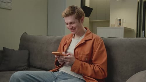 Smiling Young Adult Using Smartphone on Couch