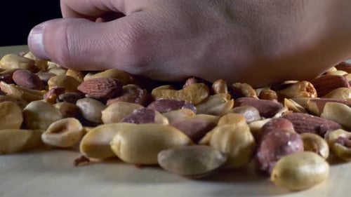 Hand Presses Mixed Nuts on Wooden Table
