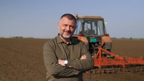 Portrait of satisfied mature farmer standing in field preparing to cultivate the land with a tractor
