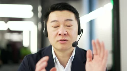 Webcam view. Asian businessman in a headset talking on a video call looking at camera sitting