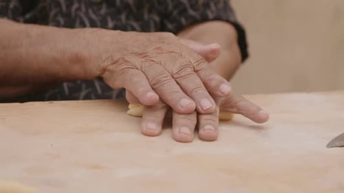An old woman's hands rolling pasta dough to make into shells in Italy.