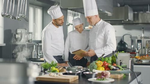 In der modernen Küche verwenden Köche das Tablet für Rezepte, sie lächeln und diskutieren.