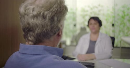 Rear view of senior male patient listening to female doctor during medical consultation in clinic,