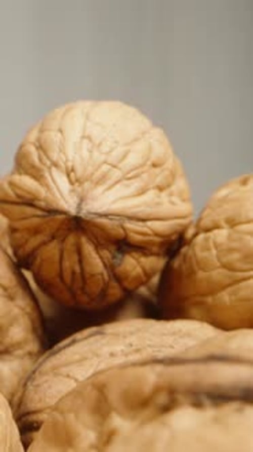 A scattering of walnuts on a white background. Dolly slider extreme close-up. Vertical video.