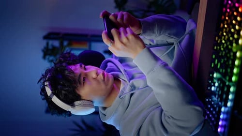 Young Adult Playing Game on Phone in Bedroom