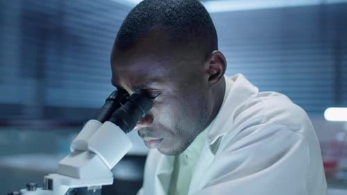 Young Adult Scientist Looks Through Microscope in Lab