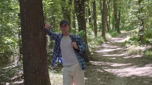 A male hiker with a backpack stands in the forest, looking up and enjoying the sounds of nature and