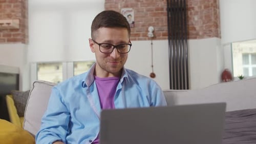 Man Uses Laptop Sitting on Couch at Home