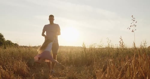 Happy Father Spinning His Daughter Holding Hands in a Golden Field at Sunset