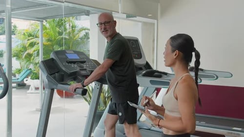 Man Walking on Treadmill at the Gym with Trainer