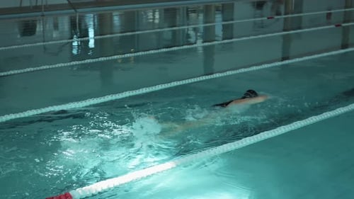 A serene image capturing a female figure swimming leisurely in an enclosed pool area with natural li