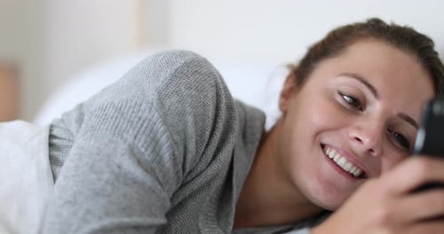 Smiling Woman Using Smartphone Lying in Bed