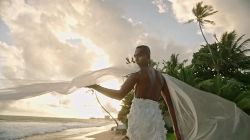 Flamboyant Gender Fluid Black Person Posing on Ocean Shore in White Chiffon Wedding Dress Nonbinary