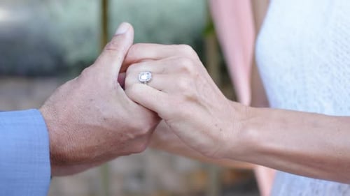 Paar nach dem Ringtausch, Mann im blauen Hemd stabilisieren die Hand einer Frau und präsentiert im Freien einen Halo-Ring