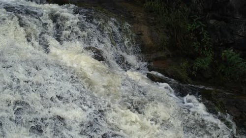 Close-up of strong waterfall current splashing over rocks, creating foam and mist in Ultra slow