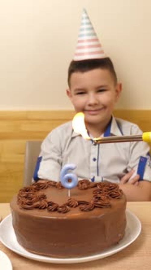 45. The boy is sitting in front of a table with a festive cake, in which a candle in the form of the