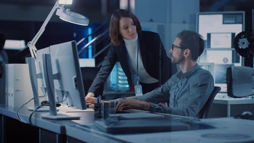 Futuristischer Entwicklungsingenieur für Maschinenmotoren arbeitet an seinem Schreibtisch am Computer und spricht mit weiblicher P