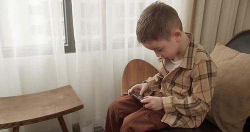Boy Using Mobile Phone While Sitting on Chair