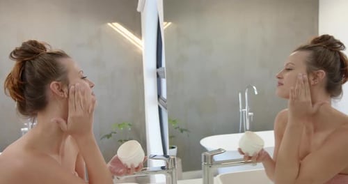 Woman Applying Moisturizer in Bathroom Mirror