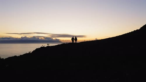 Silhouetted Figures on Hilltop at Sunrise Over Ocean