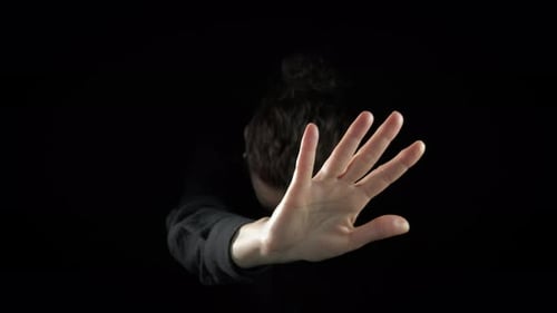 Figure Raises Hand Against Black Background