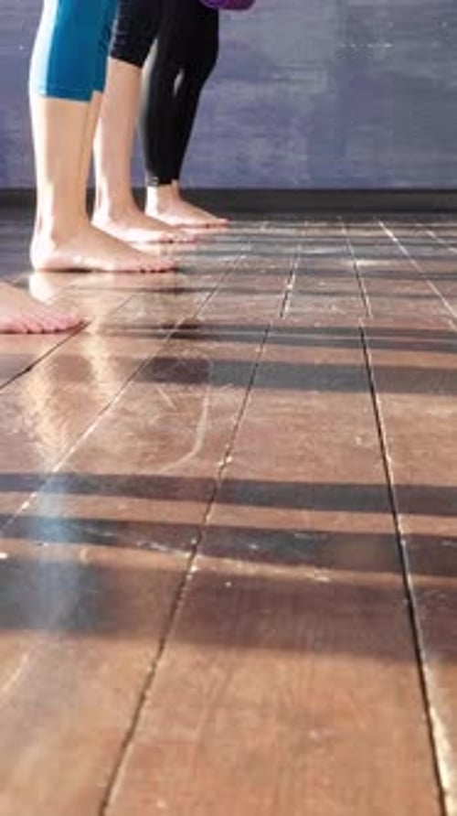 Group of Individuals Preparing Yoga Mats on Polished Wooden Floor in a Bright Studio Environment